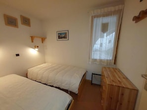 A bedroom with two beds, a wooden dresser, a window with curtains, and wall-mounted picture frames. - 10m from ski slopes, Ground floor, terrace, tv, ski locker, 27m², Valmorel (Valmorel)
