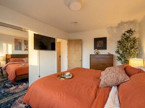 Ein Hotelzimmer mit einem großen Bett, einem Fernseher, einer Holzkommode und einer Pflanze.