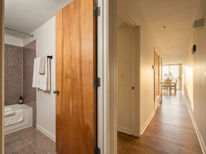 Ein Hotelzimmer mit Holztür, einem Badezimmer mit Badewanne und Handtüchern sowie einem Flur, der zu einem Essbereich führt.