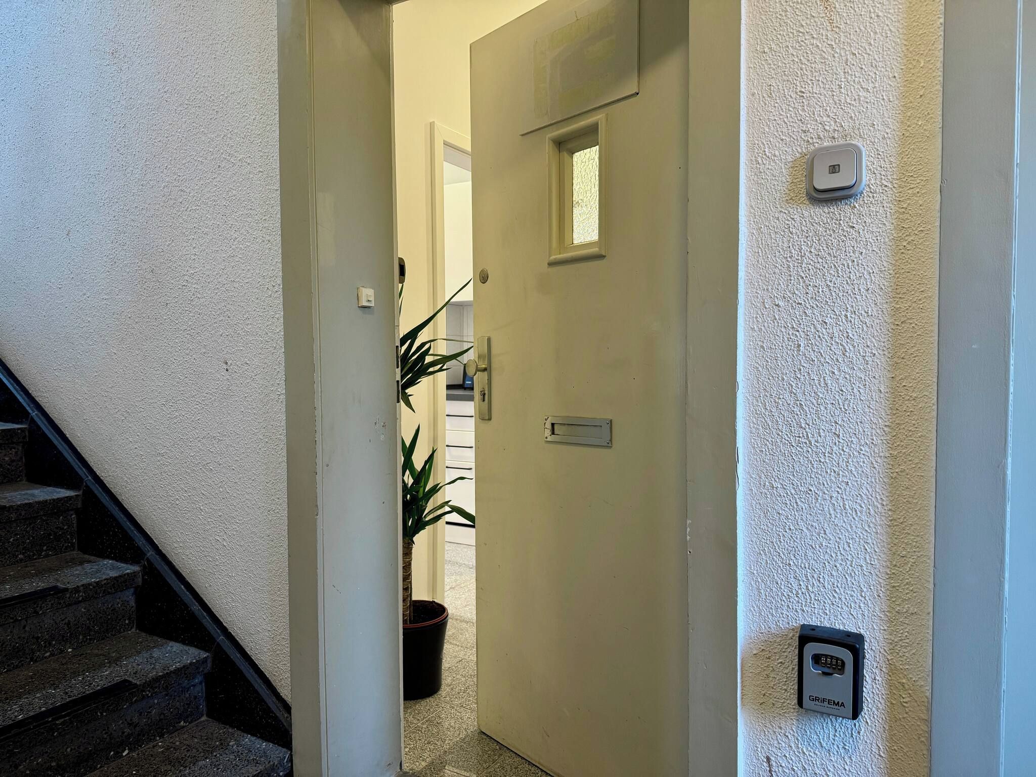 A hallway with a door, a potted plant, and a security keypad on the wall.