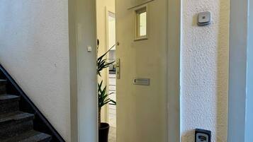 A hallway with a door, a potted plant, and a security keypad on the wall.