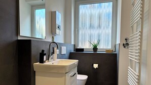 A modern bathroom with a white sink, a toilet, a mirror, and a window with a view of the outside. - Stylish Flat Central 6 Guests 65sqm (Hannover)