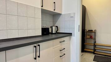 A modern kitchen with white cabinets, black handles, and a black countertop. There is a kettle on the counter and a power outlet on the wall.