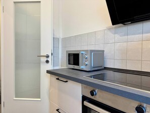 A kitchen with a microwave, a stove, and a door with frosted glass panels. - Stylish Flat Central 6 Guests 65sqm (Hannover)