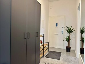 A hallway with a grey wardrobe, a wooden shelf unit, a white door, and two potted plants. - Stylish Flat Central 6 Guests 65sqm (Hannover)