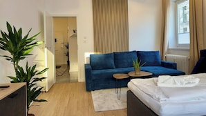 A modern hotel room with a blue sofa, a small round table, a white bed, and a potted plant. - Stylish Flat Central 6 Guests 65sqm (Hannover)