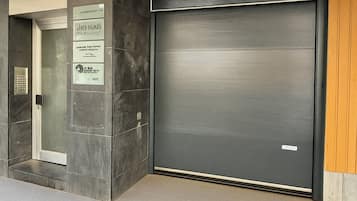 A building entrance with a closed metal shutter door, a glass door with a sign, and a tiled floor.