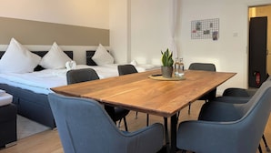 A modern hotel room with a wooden dining table, grey upholstered chairs, a bed with white bedding, and a small potted plant on the table. - Stylish Flat Central 6 Guests 65sqm (Hannover)