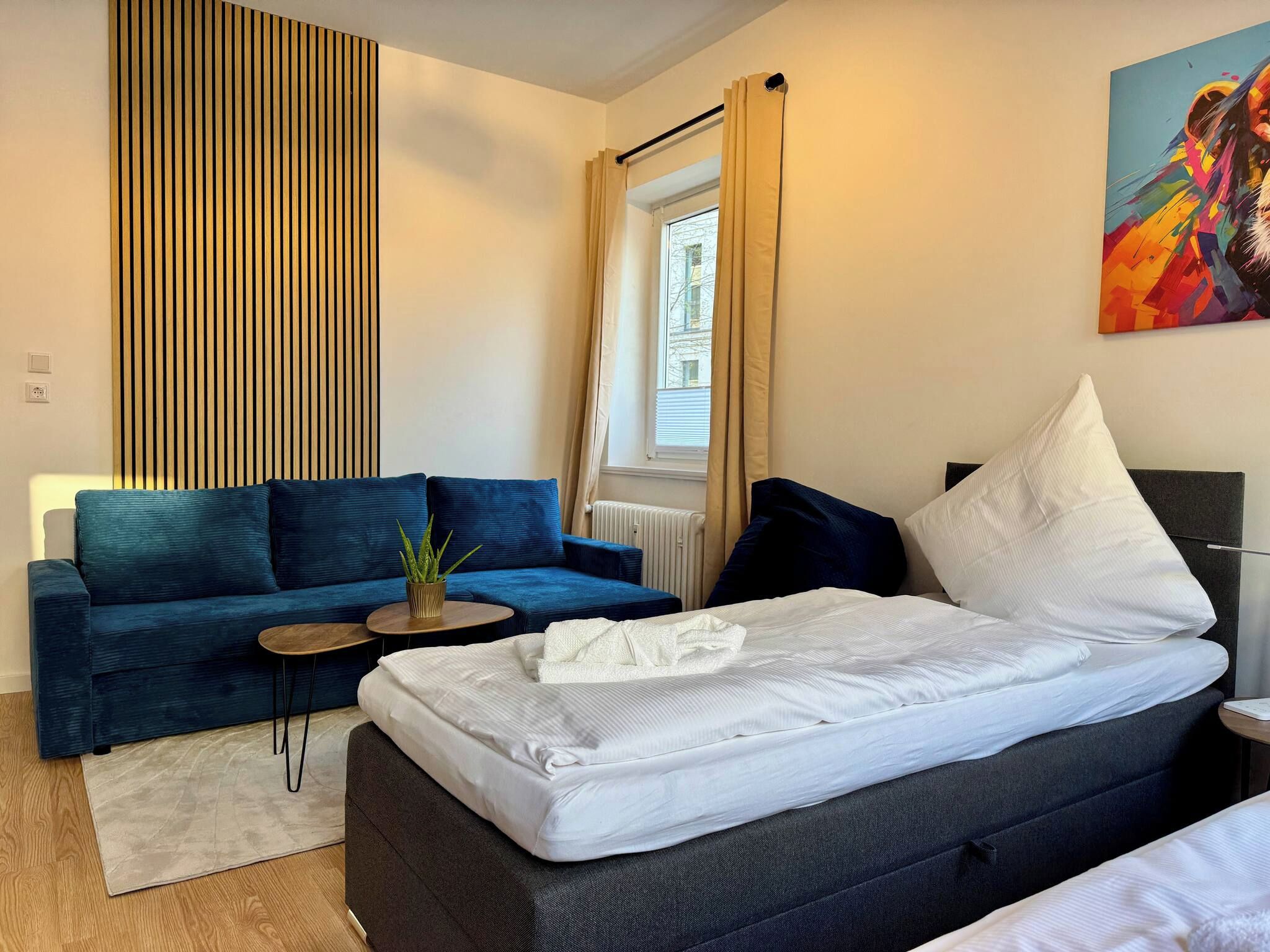 Un dormitorio moderno con una cama, un sofá, una mesita y una planta en maceta.