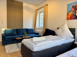 A modern bedroom with a bed, a sofa, a small table, and a potted plant. - Stylish Flat Central 6 Guests 65sqm (Hannover)