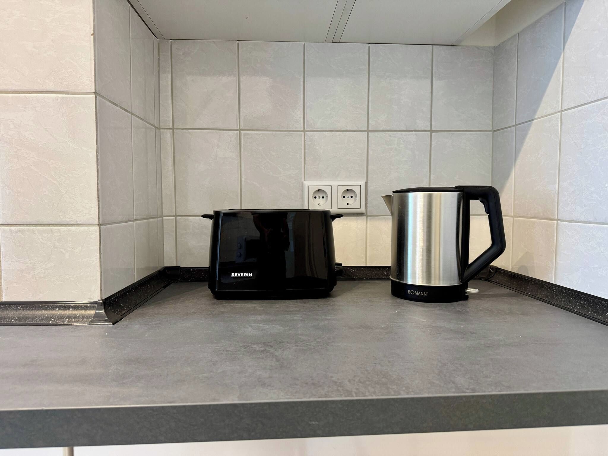 A kitchen with a coffee maker and a kettle on the counter, a power outlet, and a tiled backsplash.