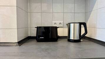 A kitchen with a coffee maker and a kettle on the counter, a power outlet, and a tiled backsplash.