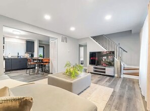 Ein modernes Wohnzimmer mit einer Couch, einem Couchtisch und einer Treppe, die in einen Essbereich führt.