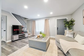 A modern living room with a flat-screen TV, a grey sofa, and a staircase. - Delightful and comfortable 4-bedroom 2-bathroom house in charming Burbank (Burbank)