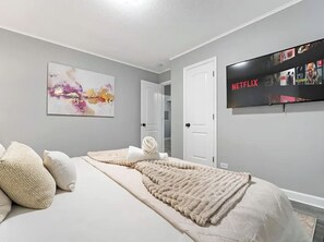Ein Schlafzimmer mit Bett, Kissen, Decke, einem an der Wand befestigten Fernseher und einer Tür.
