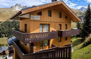 A multi-story wooden chalet with balconies, set against a mountainous backdrop. - 100m from ski slopes, floor -1, balcony, tv, ski locker, 24m², Méribel-Mottaret (Les Allues)