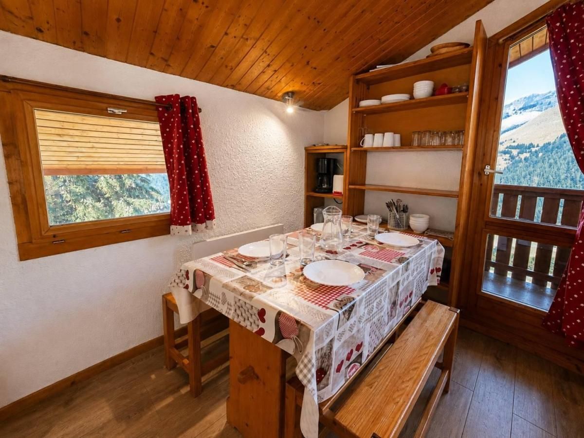 A dining area with a table set for four, wooden shelves above, and a window with a view of a mountainous landscape.