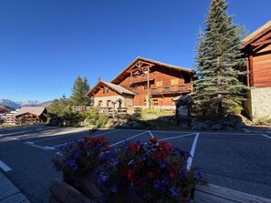 A wooden lodge with a balcony, surrounded by mountains and a parking area with flowers. - 300m from ski slopes, 1st floor, fireplace or stove, 140m², Vars (Vars)