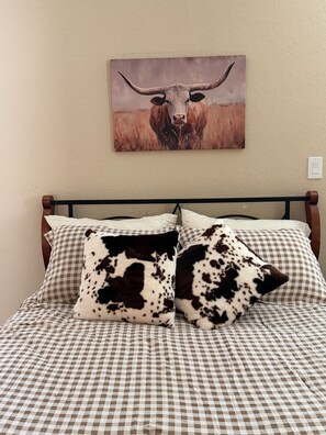 Ein Bett mit kariertem Bettbezug, zwei Küsten-Kissen und ein Bullenbild an der Wand.