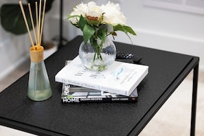 Ein Buch mit dem Titel 'The Wisdom of Nurses' auf einem schwarzen Tisch, zusammen mit einer Glaskaraffe mit weißen Blumen und einem Schilferoamparfumer.