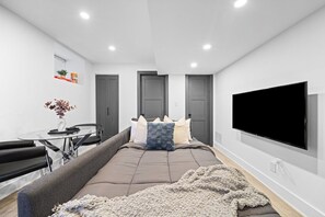A modern bedroom with a bed, a TV, a sofa, and a dining table. - Cozy Little Portugal 2BR | Sleeps 6 (Toronto)