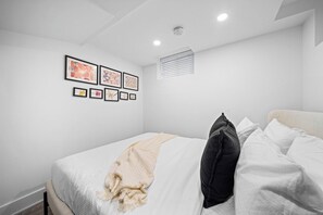 Ein Schlafzimmer mit einem Bett, weißen Wänden und gerahmten Bildern an der Wand.