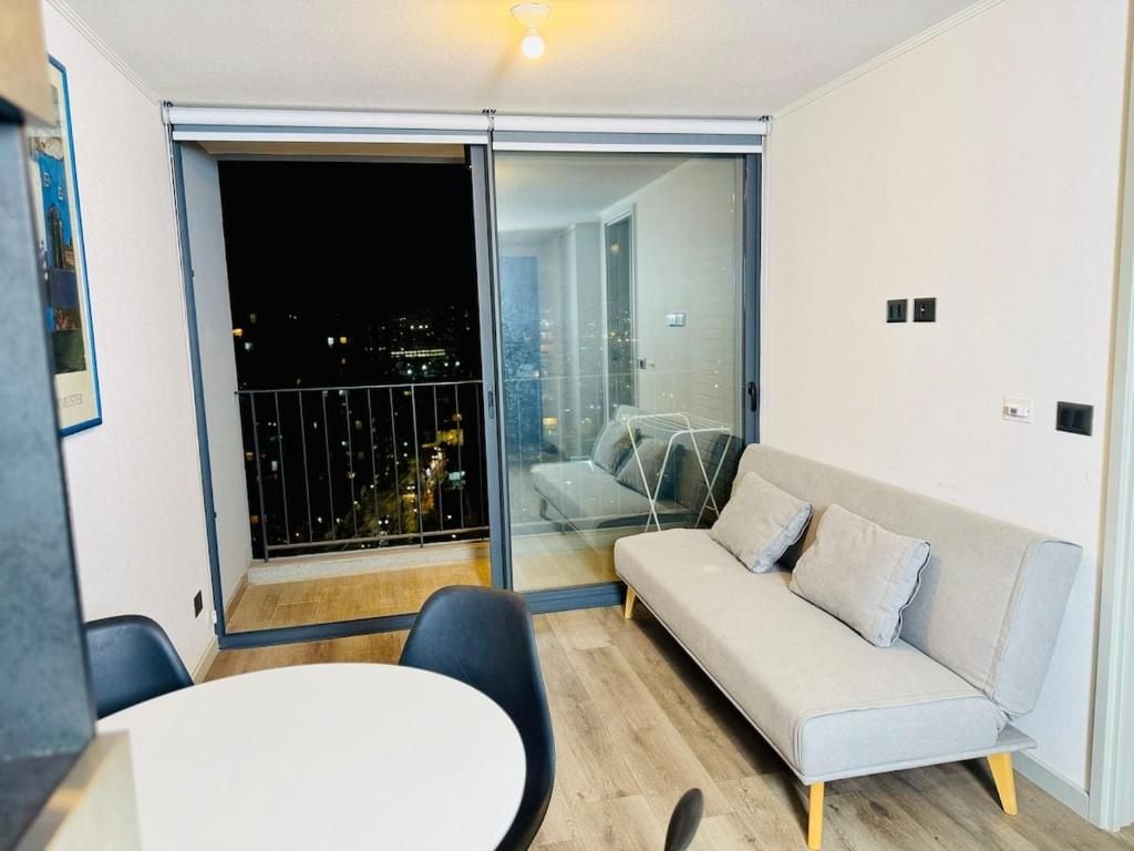 Un moderno salón con sofá, mesa de comedor y puerta corrediza de vidrio a un balcón.