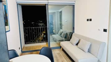 Un moderno salón con sofá, mesa de comedor y puerta corrediza de vidrio a un balcón.