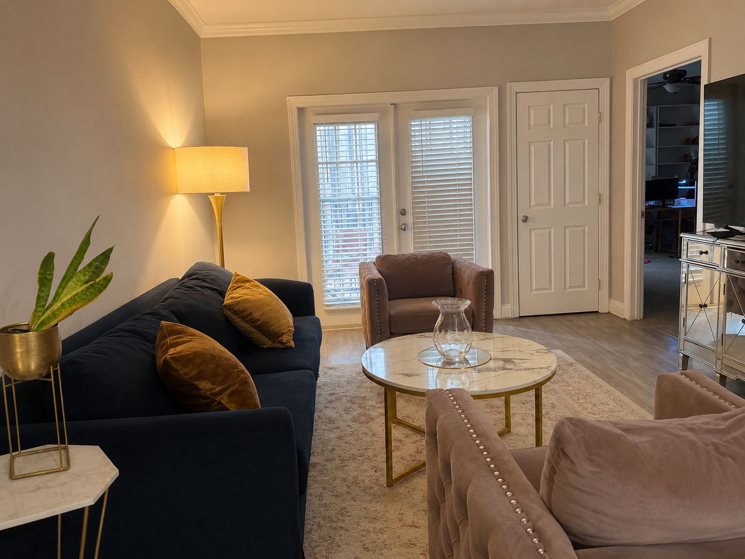 A living room with a sofa, armchairs, a coffee table, and a lamp. There are two doors and a closet visible.
