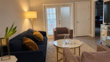 A living room with a sofa, armchairs, a coffee table, and a lamp. There are two doors and a closet visible.