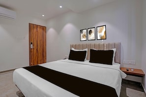 A hotel room with a bed, a wooden door, a nightstand, and three framed pictures on the wall.