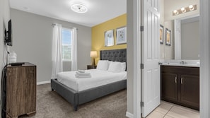 A hotel room with a bed, bedside table, lamp, and a bathroom with a mirror and sink. - Magical Disney Retreat with Pool, Spa & Theater (Kissimmee)