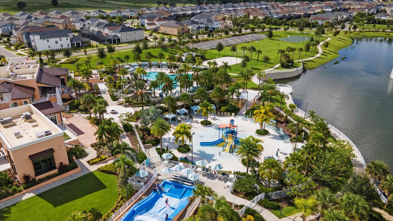 Vista aérea de una zona residencial con piscina, palmeras y un lago.