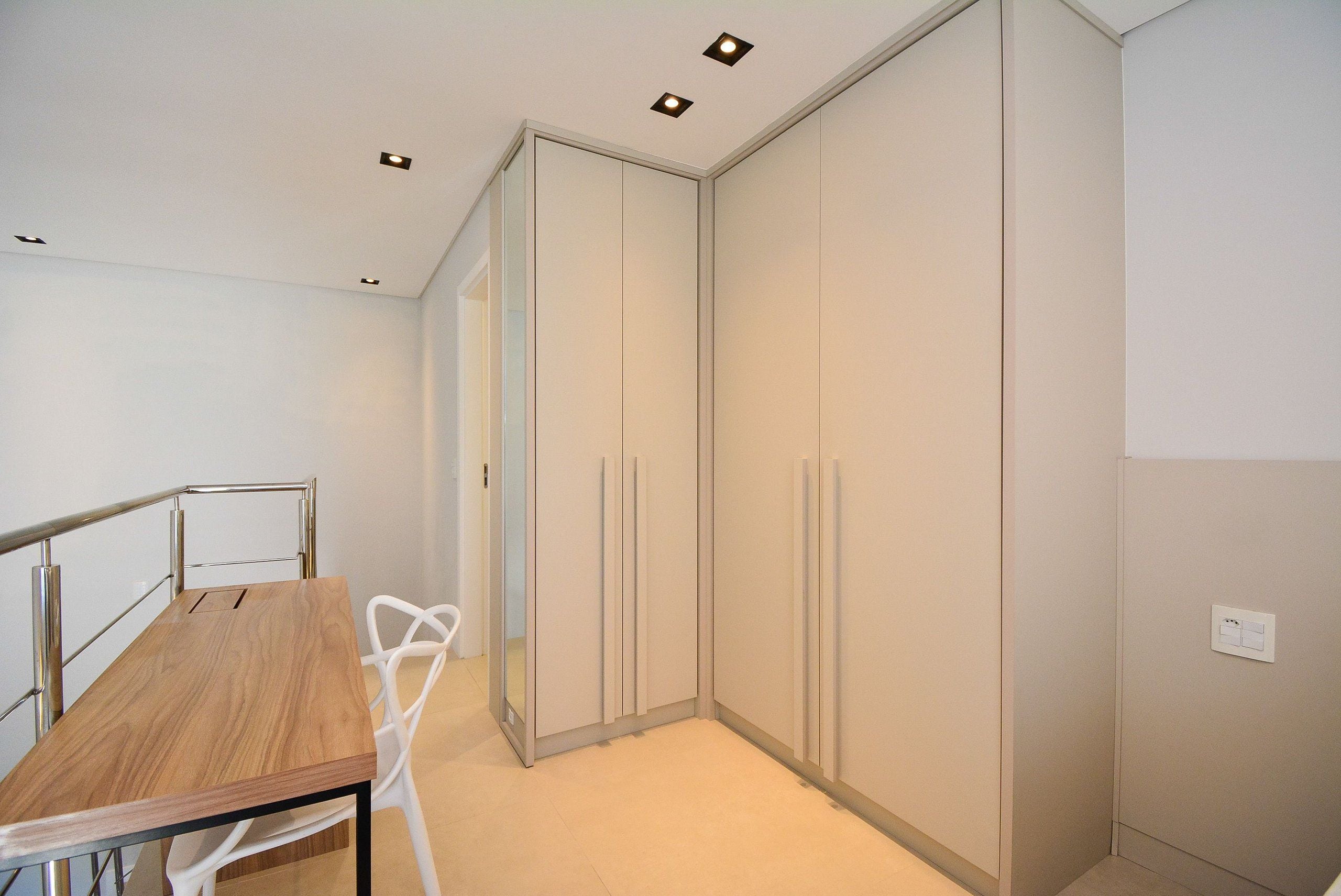 Una habitación con una mesa de madera, una silla blanca, un armario con puertas correderas e iluminación empotrada en el techo.
