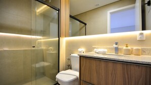 Une salle de bain moderne dotée d’une douche à parois de verre, de toilettes et d’un meuble-lavabo avec un miroir.