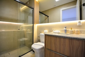 A modern bathroom with a glass shower enclosure, a toilet, and a vanity with a mirror. - Elegante Loft Sunset Lagoa - LDI006 (Florianópolis)