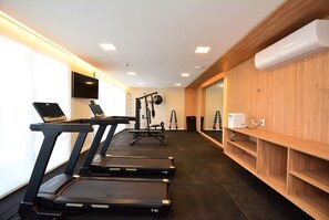 A gym with treadmills, a wall-mounted TV, and a wooden wall with a mirror and shelves. - Elegante Loft Sunset Lagoa - LDI006 (Florianópolis)