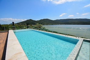 Una piscina rectangular de agua azul cristalina, rodeada por una barandilla de vidrio, con vistas a un lago y montañas al fondo.