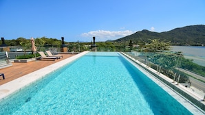 Une piscine rectangulaire à l’eau d’un bleu cristallin, entourée d’une terrasse en bois et de chaises longues.