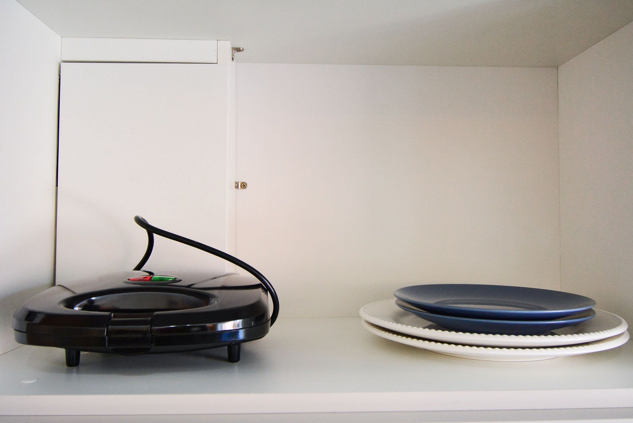 A robotic vacuum cleaner and a stack of plates on a white shelf.