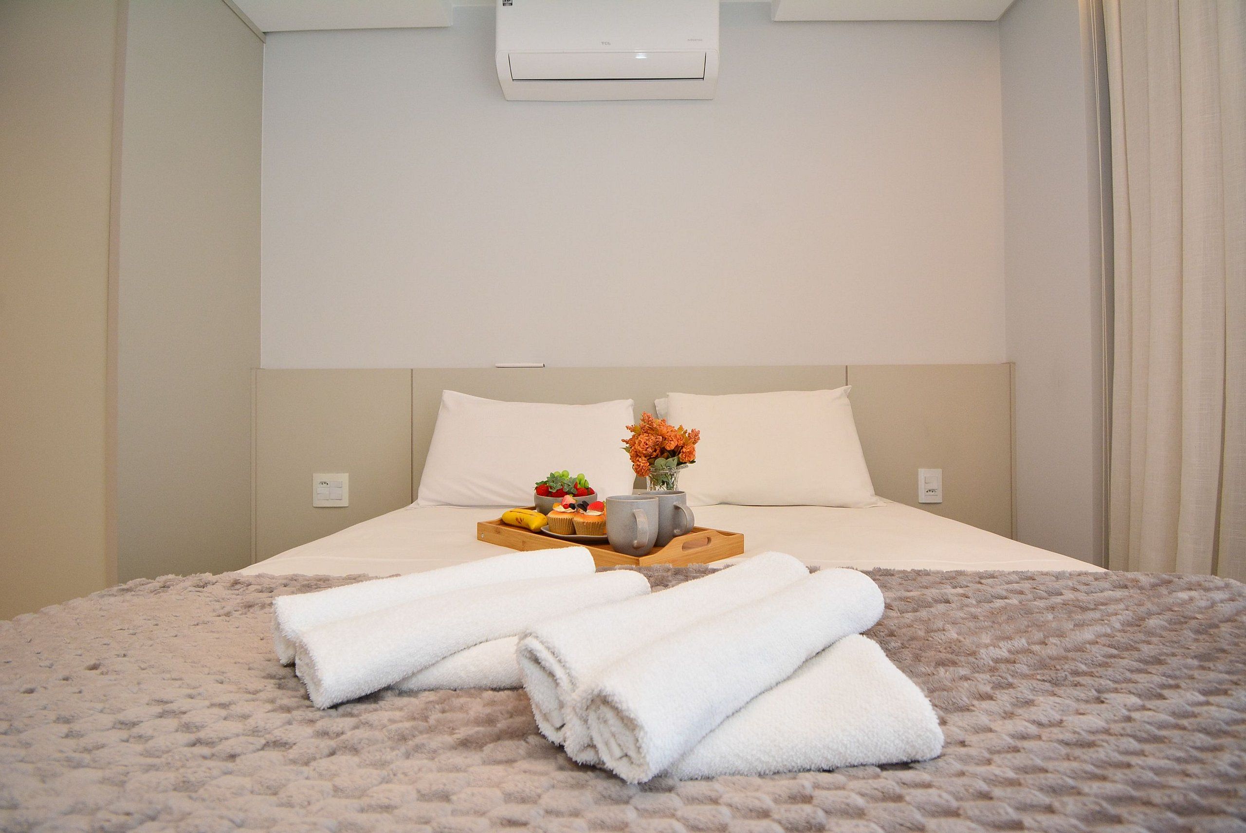 Een hotelkamer met een bed, een dienblad met bloemen en een vaas, en een witte handdoek op het bed.