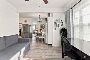 Ein modernes Wohnzimmer mit grauem Sofa, einem Essbereich mit einer Kronleuchter und einer Küche mit Kühlschrank.