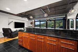 Une cuisine moderne dotée d’un grand îlot central, de meubles en bois et d’une grande fenêtre donnant sur une zone boisée.