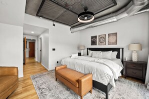 Une chambre à coucher moderne avec un lit, des tables de chevet, un banc et un couloir.
