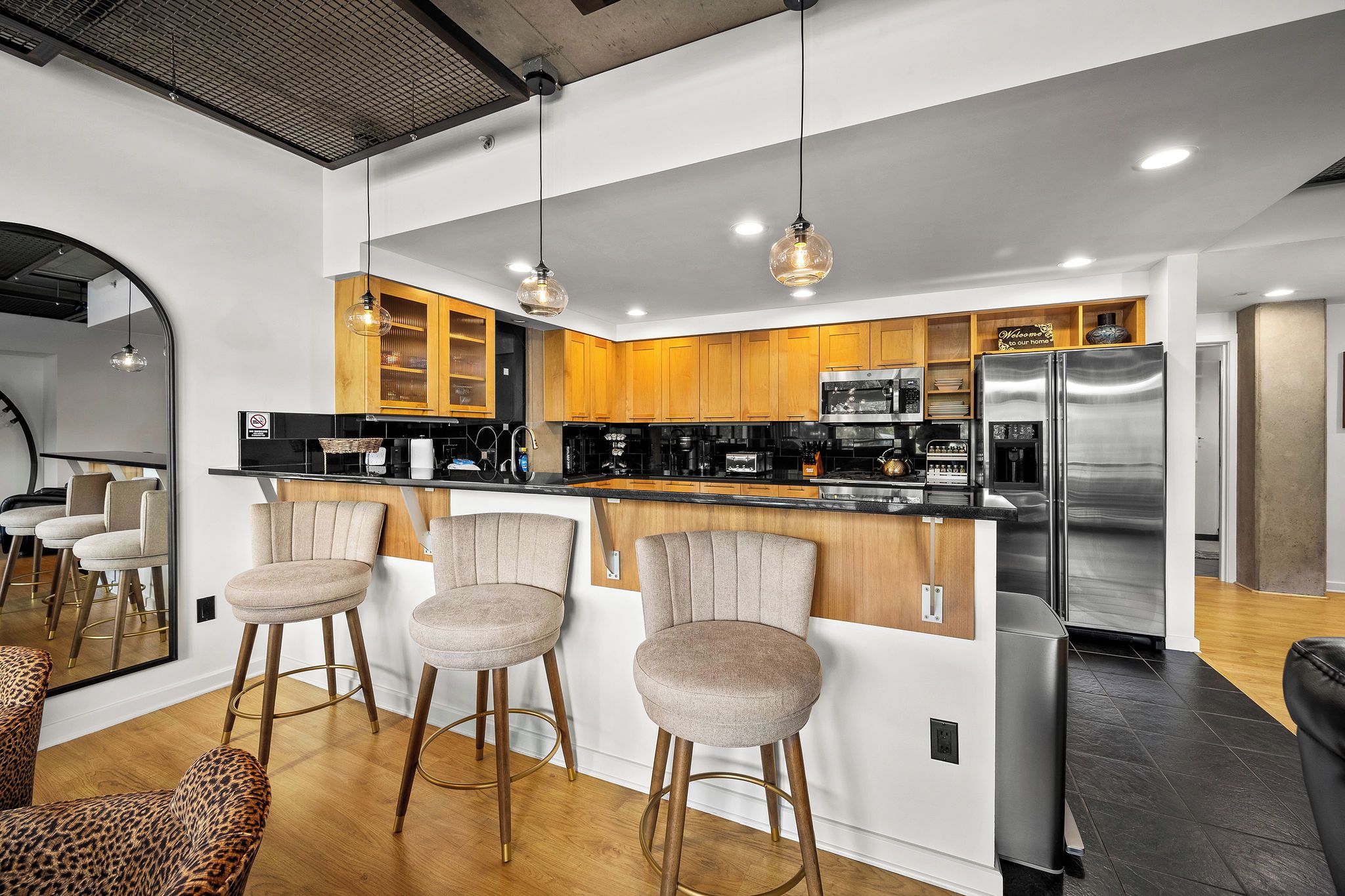 A modern kitchen with wooden cabinets, a stainless steel refrigerator, and a bar area with stools.