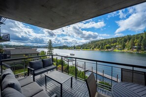 Ein Balkon mit einer Couch und einem Tisch, mit Blick auf einen See mit Booten und einen bewaldeten Hügel.