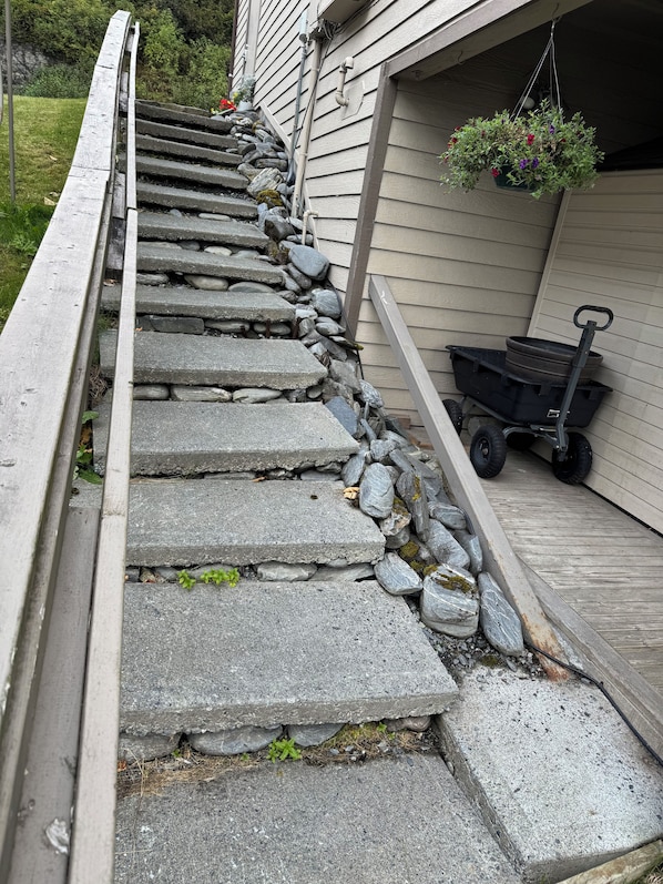 A stone staircase leading to a wooden deck area with a wheelbarrow and hanging flower pot.