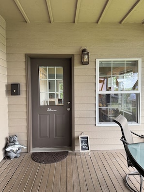A wooden deck with a dark door, a welcome sign, a lantern, and a chair.