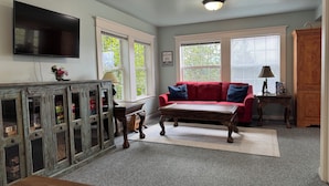 A living room with a red sofa, a television mounted on the wall, and a wooden cabinet with glass doors. - Breathtaking mountain view, private entrance, romantic getaway (Valdez)