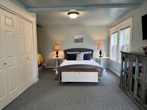 A bedroom with a bed, two bedside tables, a nightstand, a dresser, and a window with a view.